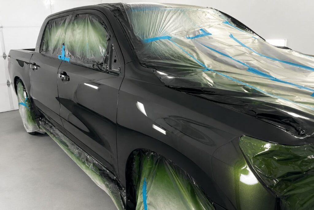 A pickup truck professionally masked and prepared for side panel painting and refinishing inside the paint booth at UK Body Work in Hyannis, Massachusetts.